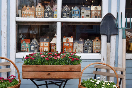 Shop window display of miniature houses and spring flowers with garden tools outside cottage store.
