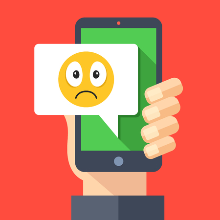 Hand holding smartphone with sad emoji message on screen. Sad emoticon icon. Social networking, instant messaging on mobile device, online chat concepts. Modern flat design vector illustrationのイラスト素材