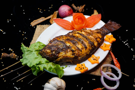 grilled fish with sauce and vegetables on a black background in restaurantの写真素材