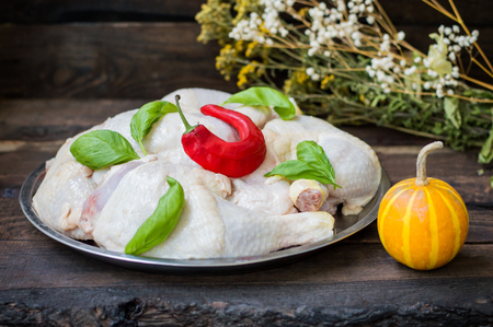Raw chicken legs on a tray with a red hot pepper and basil. Wooden backgroundの写真素材