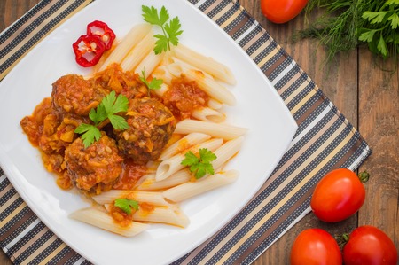 Meatballs with pasta penne in tomato sauce on a white plate. Wooden rustic background. Top view.の写真素材