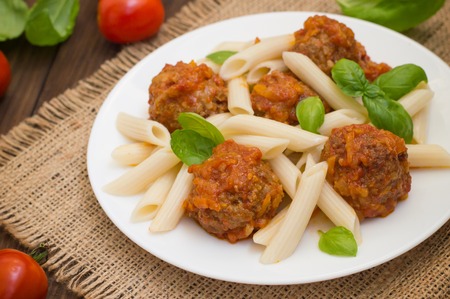 Meatballs with pasta penne in tomato sauce on a white plate. Wooden rustic background. Top view.の写真素材