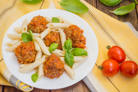 Meatballs with pasta penne in tomato sauce on a white plate. Wooden rustic background. Top view.の写真素材