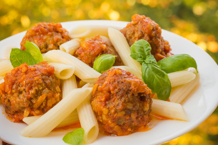 Meatballs with pasta penne in tomato sauce on a white plate. Wooden rustic background. Top view.の写真素材