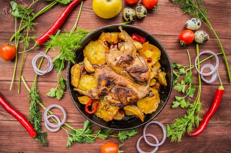 Quail baked in a pan with potatoes and apples. On a brown wooden background. Top viewの写真素材