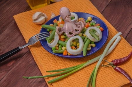 Octopus and squid rings on fresh vegetables on the blue plate on a wooden background. Top viewの写真素材