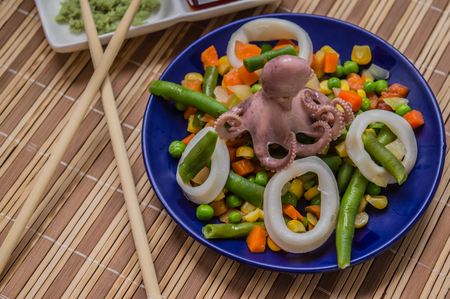 Octopus and squid rings on fresh vegetables on the blue plate on a wooden backgroundの写真素材