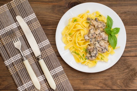 Fettuccine pasta in a creamy sauce with mushrooms on a plate on a wooden table. Horizontal top viewの写真素材