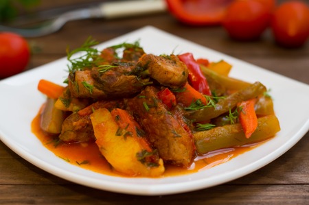 Stew with potatoes, carrots, pickles, tomatoes and hot peppers. Azu by Tartarian on a white square plate. Wooden rustic background. Top viewの写真素材