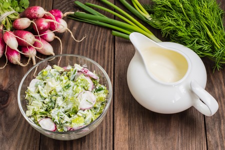 Salad with radishes, lettuce, spinach and sour cream on a wooden tableの写真素材