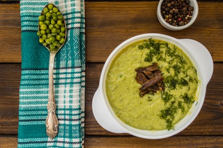 Puree soup with peas, melted cheese, roasted meat, croutons and herbs. Wooden background. Top viewの写真素材