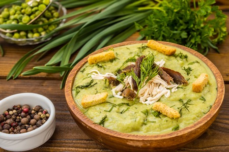 Puree soup with peas, melted cheese, roasted meat, croutons and herbs. Wooden background. Top viewの写真素材