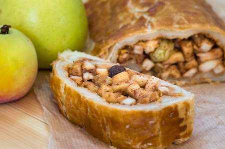 Apple strudel with fresh apples, nuts and powdered sugar on a wooden background. Close-up
