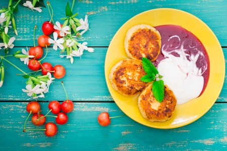 Cheese pancake with jam and fresh cherries. Wooden turquoise background. Close-up. Top viewの写真素材