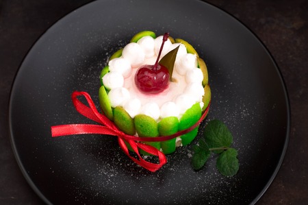 Fruit dessert tart with whipped sweet curd cream and with sweet cherry on top. Old black background. Top view. Close-upの写真素材