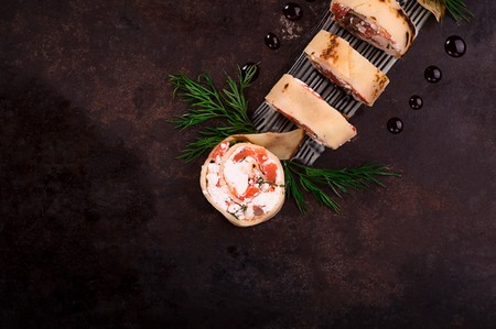 Rolls of thin pancakes with salmon, horseradish cream cheese. Black old background. Top view....