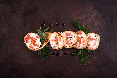 Rolls of thin pancakes with salmon, horseradish cream cheese. Black old background. Top view. Selective focusの写真素材