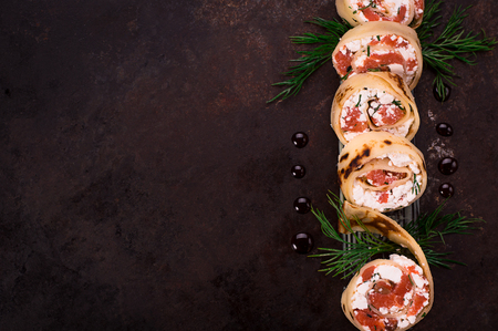 Rolls of thin pancakes with salmon, horseradish cream cheese. Black old background. Selective focus. Top viewの写真素材