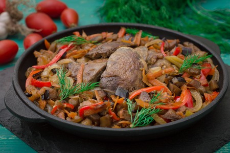 Fried chicken liver with vegetables and herbs in the frying pan. Wooden turquoise background. Top view.の写真素材