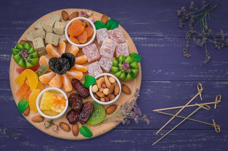 Set of eastern desserts. Marmalade, kivi, prunes, rahat lokum, nuts, mandarin, persimmon, dried apricots, pistachios, dates raisins in a colorful blue Wooden rustic background Top viewの写真素材