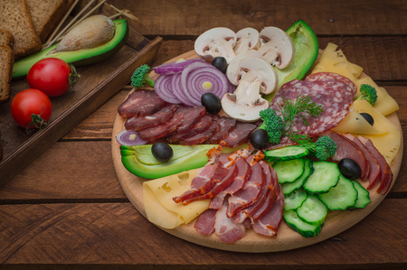 Cold smoked meat with prosciutto, salami, bacon, pork chops, cheese, mushrooms, cucumber, avocado, onion and olives Wooden rustic background Top viewの写真素材