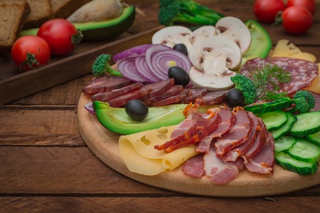 Cold smoked meat with prosciutto, salami, bacon, pork chops, cheese, mushrooms, cucumber, avocado, onion and olives Wooden rustic background Top viewの写真素材