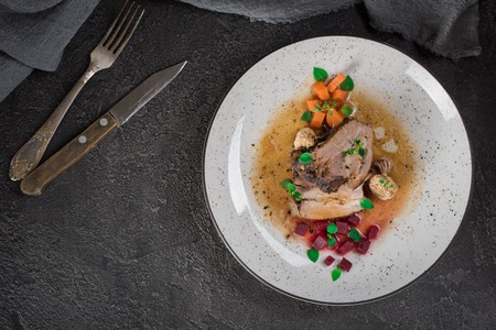 Pork ribs with beets, carrots, fried mushrooms and sauce on a white plate. Restaurant serving. Old black rustic background. Top view.の写真素材