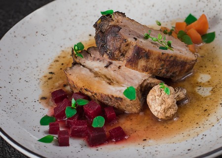 Pork ribs with beets, carrots, fried mushrooms and sauce on a white plate. Restaurant serving. Old black rustic background. Top view.の写真素材