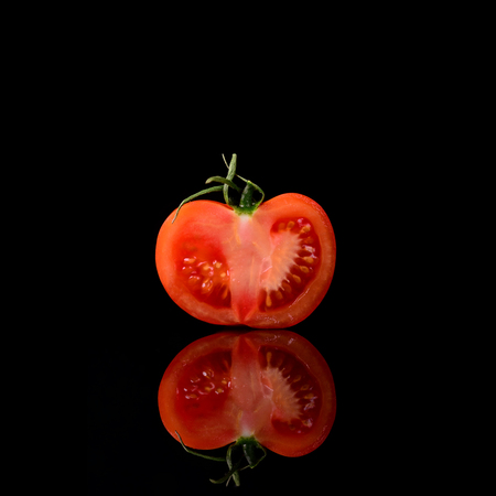 Tomato isolated on the black and glossy background with realistic reflection and water dropsの写真素材