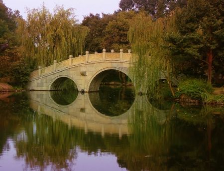 Ancient stone bridge, sky and trees reflecting in the waters of a West Lake park in Hangzhou Chinaの写真素材