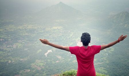 Young man standing outdoors raising his hands enjoying nature view. Relaxing, freedom and wellness concept.の写真素材