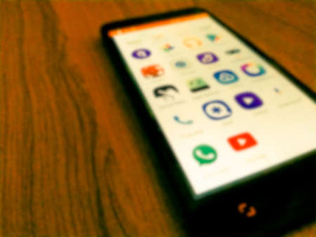 Social media app icons shows on screen of smartphone. wooden textured background.related blur.