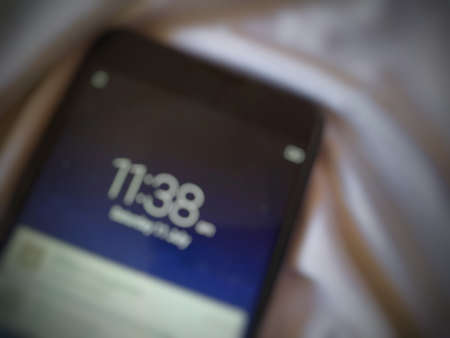 Time and date showing in smartphone rest on white silk cloth.blurred.