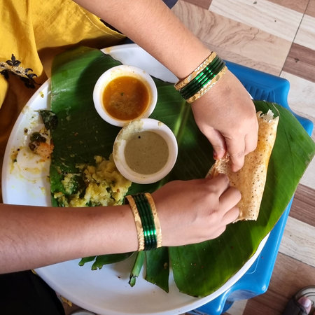 Hands of a young woman eating fresh and healthy dining dish breakfast in a banana leaf on table.