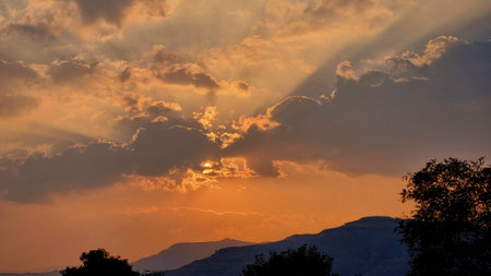 Sun behind dramatic clouds with sunray sky above the mountain rangeの写真素材