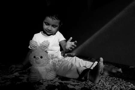 Indian girl child holding doll in W shape sitting position in low key light monochrome photo, Kalaburagi, Karnataka/India-October 09 2020のeditorial素材
