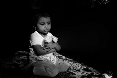 Indian girl child holding doll in W shape sitting position in low key light monochrome photo, Kalaburagi, Karnataka/India-October 09 2020のeditorial素材