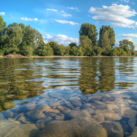 Lake with stony shallow water zone and trees on the shore