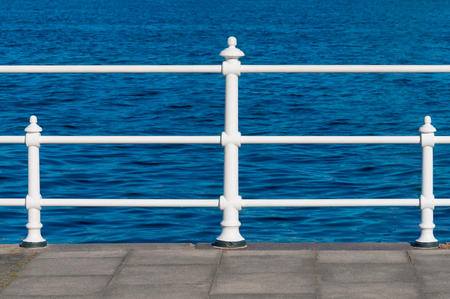 White laquered railing at port's border in front of deep blue sea; Maritine scenery; Walk on beach boardwalkの写真素材