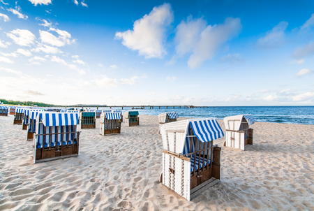 Sandy beach on the Baltic coast with locked beach chairs in the early morning; Beach furnitures in the sand; White, roofed wicker chairs with blue-white cover; Maritime sceneryの写真素材