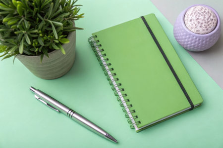 Green notebook with pen and flowerpot on green and white background.の素材