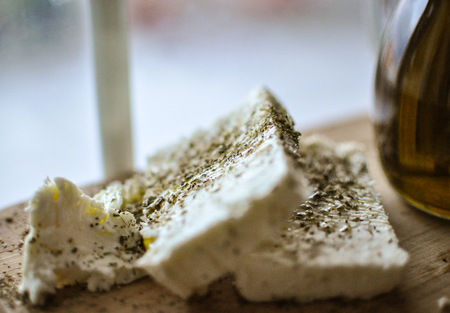 close up of feta cheese(Greek cheese) slices on a wooden serving board and a bottle of olive oil in nature lightの写真素材