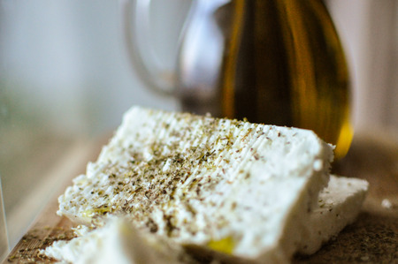 close up of feta cheese(Greek cheese) slices on a wooden serving board and a bottle of olive oil in nature lightの写真素材