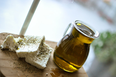 close up of feta cheese(Greek cheese) slices on a wooden serving board and a bottle of olive oil in nature lightの写真素材