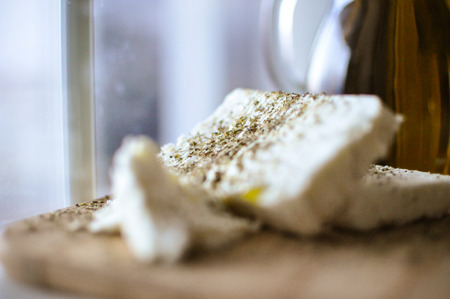 close up of feta cheese(Greek cheese) slices on a wooden serving board and a bottle of olive oil in nature lightの写真素材