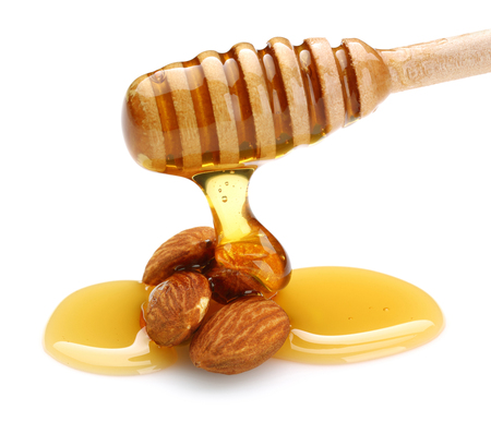 Honey dripping from dipper, on almonds isolated on white backgroundの写真素材