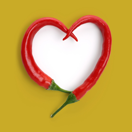 Heart shape made of red peppers, isolated on mustard colour backgroundの写真素材