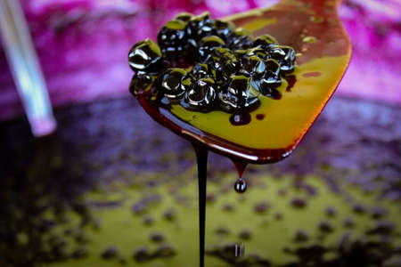 A group of chokeberry berries on a wooden cooking spoon, liquid jam leaks and drips down the spoon...
