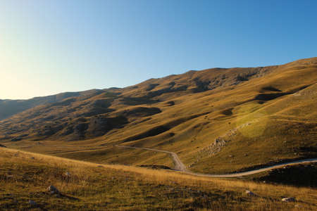 Road through the unevenness of the Bosnian mountain Bjelasnica. The grass in autumn gives a yellow...