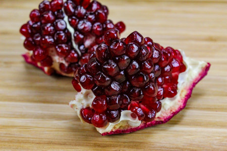 Two pieces of pomegranate with red seeds on a wooden tray. Pomegranate seeds. One piece in front and the other piece of ripe pomegranate fruit behind.の写真素材